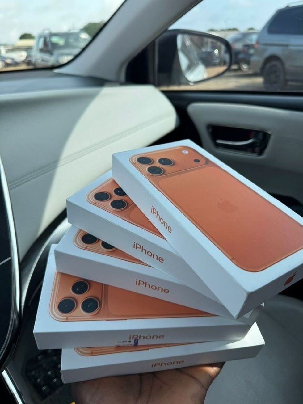 Várias caixas de iPhone laranja seguradas na mão dentro de um carro